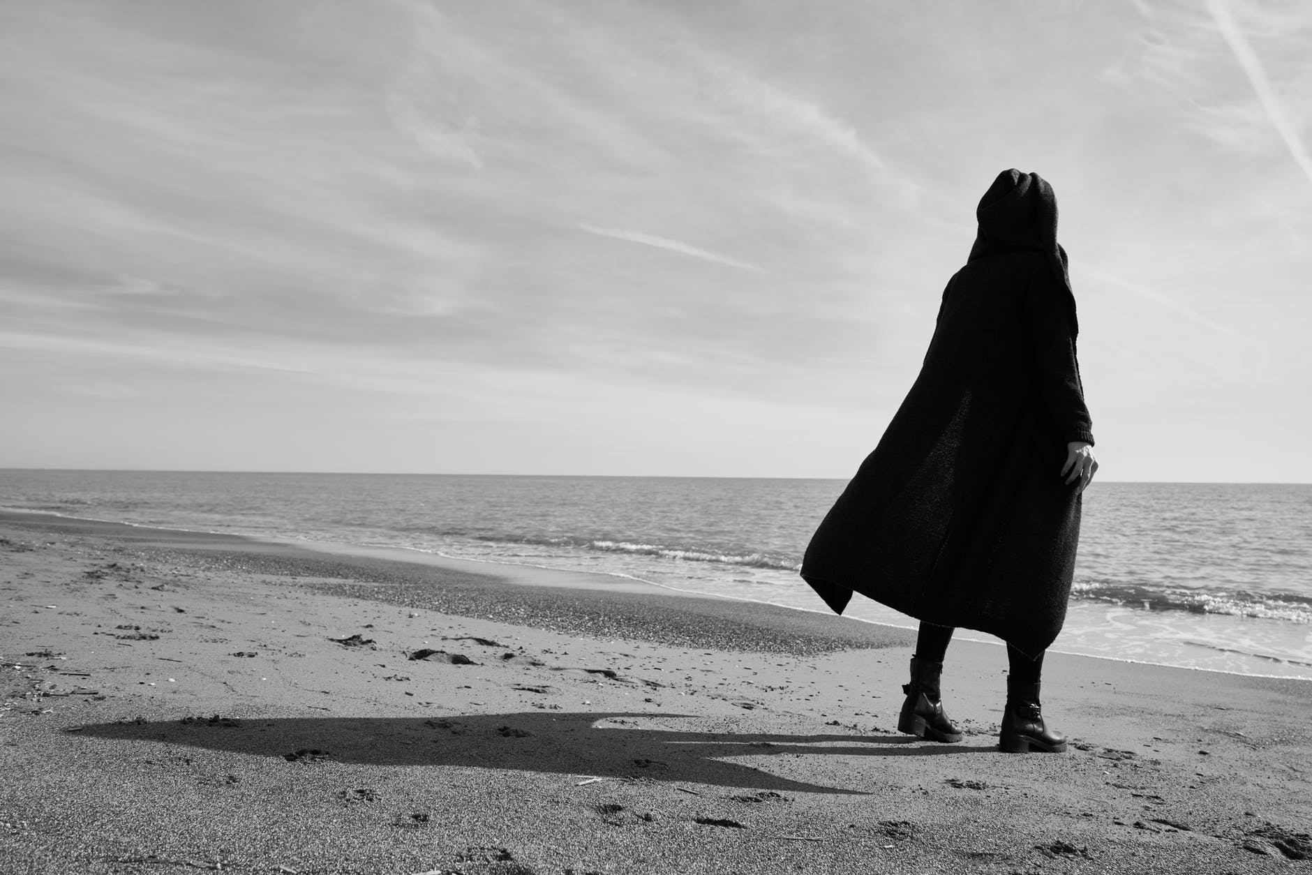 grayscale photo of person standing on seashore