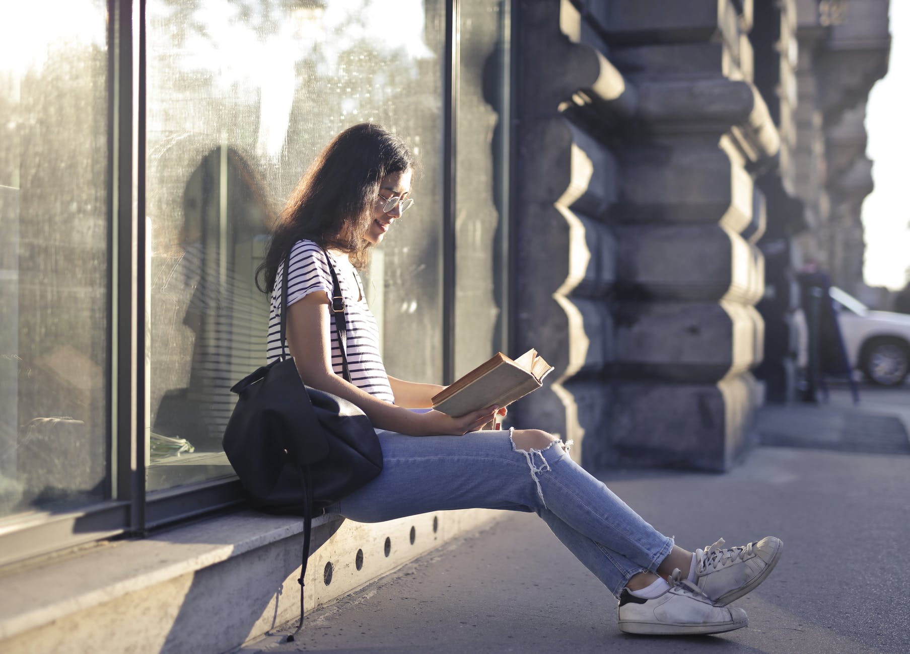 woman sitting near glass wall while reading a book