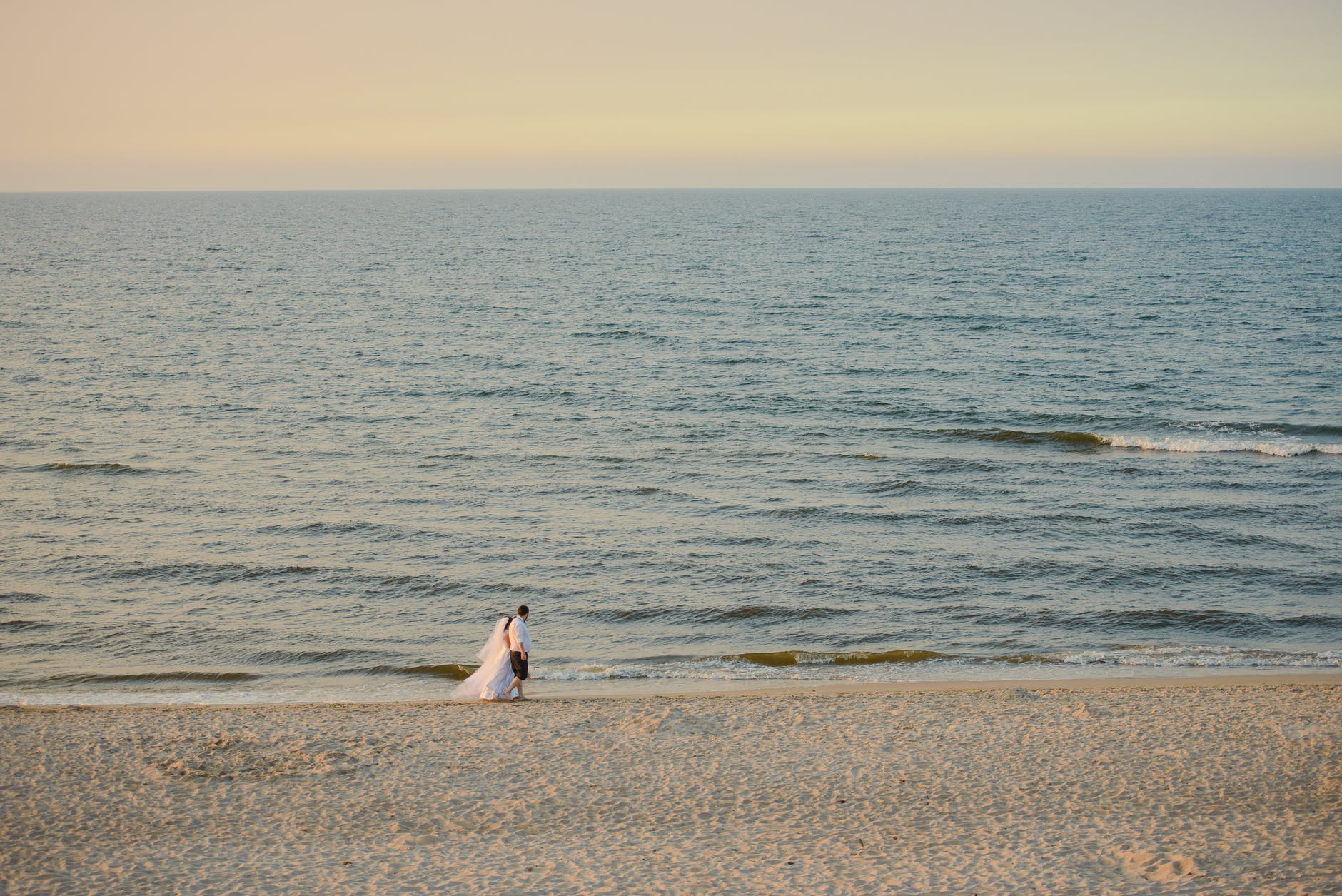 anonymous newlyweds walking on sandy beach