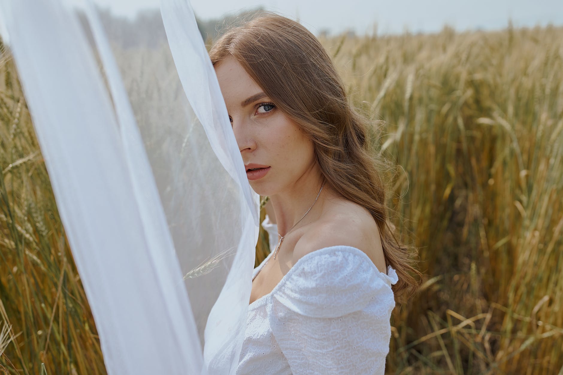 beautiful woman standing on grassy meadow near waving veil